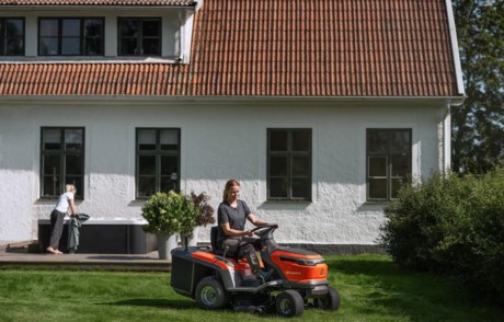Kvinna som klipper gräset med en batteridriven Husqvarna trädgårdstraktor